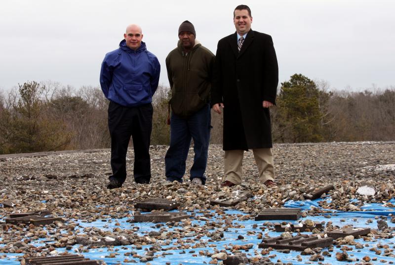The school department is seeking a debt exclusion to fund repairs to the high school roof. In this photo, Wareham High School Athletic Director Marc Loranger, Head Custodian René Nascimento, and Principal Scott Palladino stand on the high school gymnasium's roof, where staffers have covered a leaking section with a big sheet of tarp. BY JAIME REBHAN